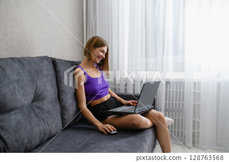 Young woman working on laptop while sitting on sofa at home. Young woman working on laptop while sitting on sofa at home. 128763568