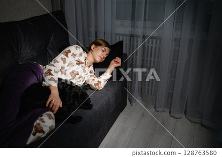 Young woman sleeping on sofa cuddling black cocker spaniel puppy. Young woman sleeping on sofa cuddling black cocker spaniel puppy. 128763580