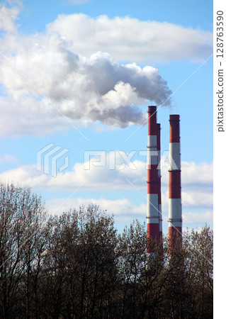 Industrial smokestacks release clouds of smoke against a blue sky, showcasing environmental impact on a sunny day 128763590