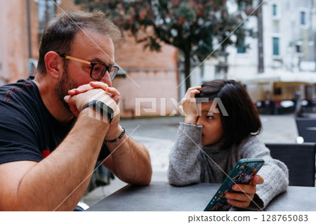daughter and a father sitting at the table outdoors and talking 128765083