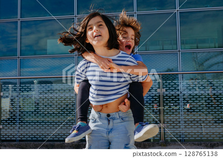 girl in striped t-shirt and jeans jumping with smaller girl carried on her back 128765138