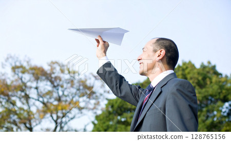 Horizontal composition of a man in a suit lightly throwing a white paper airplane 128765156