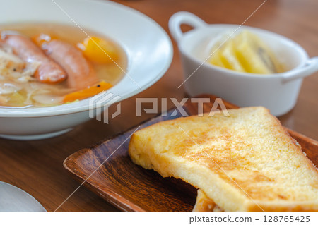 A breakfast table with French toast, vegetable soup, and fruit yogurt 128765425