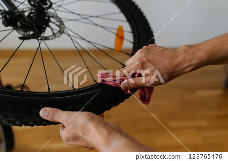 Bike mechanic cleaning tire of bicycle wheel with cloth, ensuring optimal performance and maintaining bike pristine condition in professional workshop, close-up. Concept of bike maintenance, service. Bike mechanic cleaning tire of bicycle wheel with cloth, ensuring optimal performance and maintaining bike pristine condition in professional workshop, close-up. Concept of bike maintenance, service. 128765476