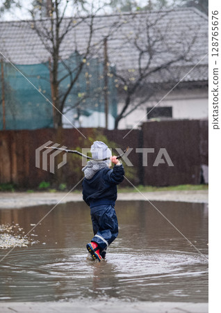 Happy Child Jumping in Rainy Puddle Outdoor Fun in Waterproof Clothes Happy Child Jumping in Rainy Puddle Outdoor Fun in Waterproof Clothes 128765676