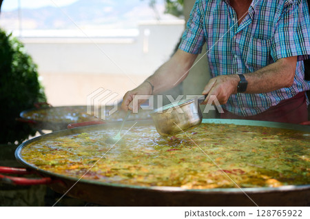 Chef Preparing Traditional Paella at an Outdoor Spanish Village Celebration Event Chef Preparing Traditional Paella at an Outdoor Spanish Village Celebration Event 128765922
