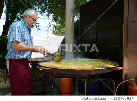 Chef Preparing Traditional Paella Outdoors in a Spanish Village Chef Preparing Traditional Paella Outdoors in a Spanish Village 128765924