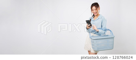 Basket in hand, shopping Asian woman holding mobile phone at supermarket shopping checklist shows online grocery convenience and happy lifestyle. isolated studio white background Basket in hand, shopping Asian woman holding mobile phone at supermarket shopping checklist shows online grocery convenience and happy lifestyle. isolated studio white background 128766024