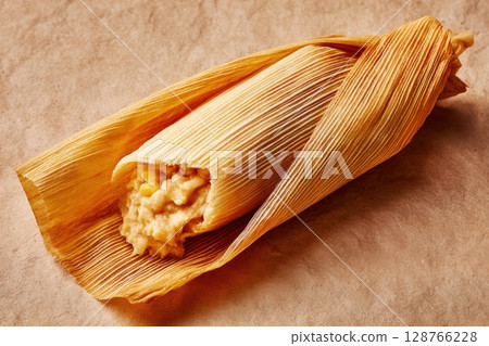 Partially Opened Tamale in Corn Husk on Beige Background Partially Opened Tamale in Corn Husk on Beige Background 128766228