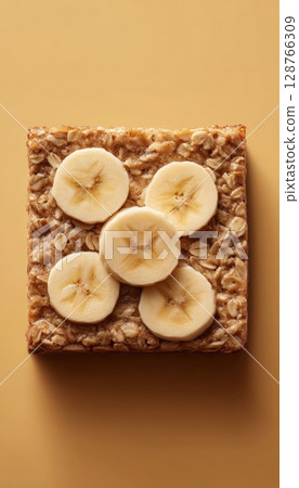 Baked Oatmeal Square with Banana Slices on Warm Background 128766309