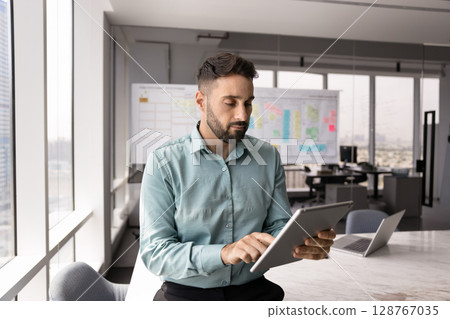 Young 30s Hispanic man engaged in work-related workflow using tablet Young 30s Hispanic man engaged in work-related workflow using tablet 128767035