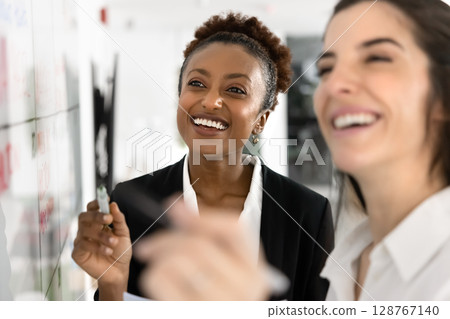Two happy women creating visual representation of goals on whiteboard Two happy women creating visual representation of goals on whiteboard 128767140