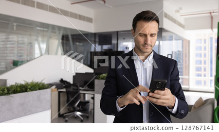 Serious businessman dressed in suit holds smartphone 128767141