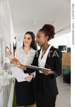 Two multiethnic women colleagues make data analysis, develop marketing strategy 128767206
