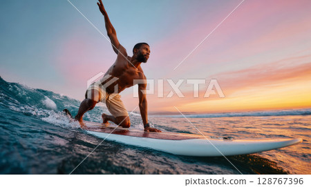 Athletic Black man surfing ocean wave during colorful sunset with skill and determination 128767396