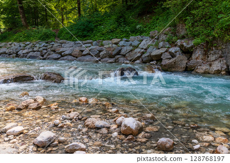 Clear alpine stream with turquoise water flowing over smooth stones near a forest trail in Garmisch-Partenkirchen, Bavaria. A peaceful nature scene perfect for outdoor and travel themes. 128768197