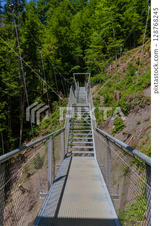 Steel suspension bridge on a forest trail near Partnachklamm, Garmisch-Partenkirchen, Bavaria. A modern walkway offering stunning views of pristine alpine nature and lush green woodland. 128768245