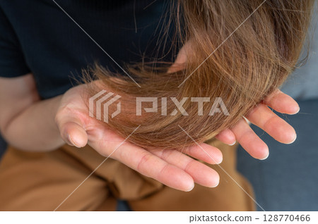 Cropped shot view of Asian woman holding her damaged split ended hair. Hair damage is risk for further damage and breakage. It may also look dull or frizzy and be difficult to manage. 128770466