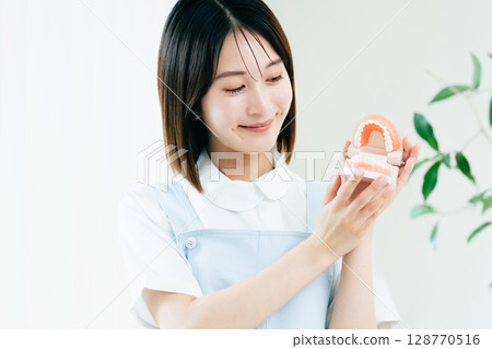 Dental staff woman holding a tooth model Dental staff woman holding a tooth model 128770516