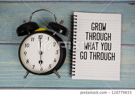 Grow Through What You go Through text written on notepad with alarm clock on wooden background 128770655