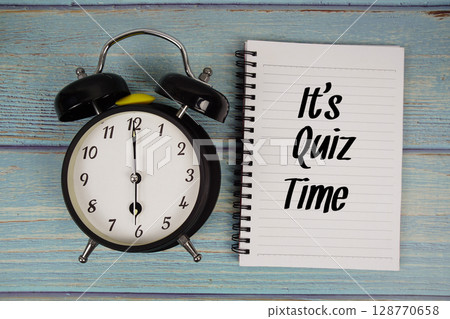 It's Quiz Time text written on notepad with alarm clock on wooden background 128770658
