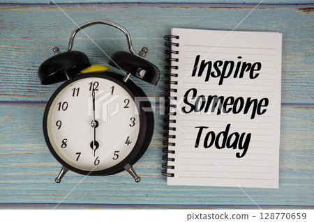 Inspire Someone Today text written on notepad with alarm clock on wooden background 128770659