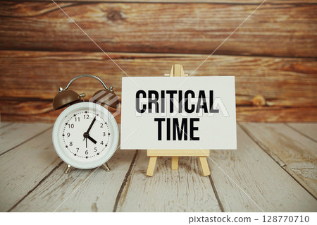 Critical Time text with easel and alarm clock on wooden background Critical Time text with easel and alarm clock on wooden background 128770710