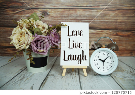 Love Live Laugh text with easel and alarm clock on wooden background 128770715