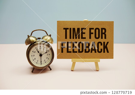 Time For Feedback text with easel and alarm clock on blue and pink background 128770719