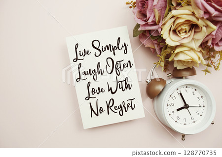 Live Simply Laugh Often Love With No Regret text on paper card with alarm clock on pink background Live Simply Laugh Often Love With No Regret text on paper card with alarm clock on pink background 128770735