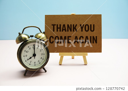 Thank you come again text on paper card with alarm clock on pink background 128770742