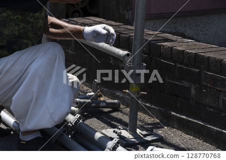 Workers assembling scaffolding 128770768