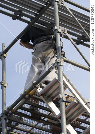 Workers assembling scaffolding 128770843