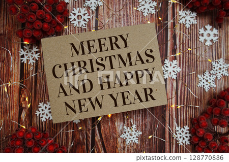 Merry Christmas and Happy New Year text on paper card with Snowflek and LED light decoration on wooden background Merry Christmas and Happy New Year text on paper card with Snowflek and LED light decoration on wooden background 128770886