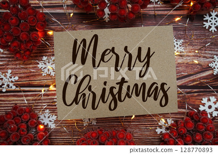 Merry Christmas text on paper card with Snowflek and LED light decoration on wooden background Merry Christmas text on paper card with Snowflek and LED light decoration on wooden background 128770893