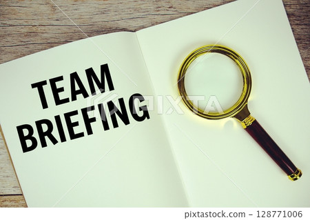 Team Briefing text message written on paper note with magnifying glass top view on wooden background 128771006
