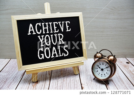 Achieve Your Goals text written on chalkboard with alarm clock on wooden background Achieve Your Goals text written on chalkboard with alarm clock on wooden background 128771071