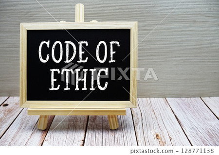 Code Of Ethic text written on chalkboard with easel on wooden background 128771138