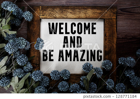 Welcome and Be Amazing text with flowers decoration on wooden background 128771184
