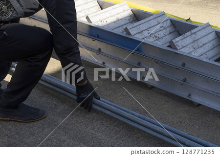 Assembling the scaffolding: Workers unloading materials from a truck and preparing them 128771235