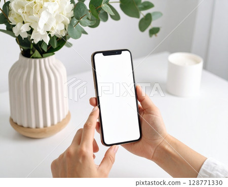 A woman's hand operating a smartphone on a white table 128771330