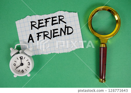 Refer A Friend text written on paper with magnifying glass and alarm clock 128771643