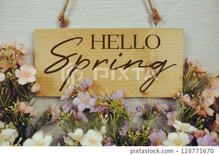 Hello Spring text on wooden sign hanging and flowers decorated on white brick wall background Hello Spring text on wooden sign hanging and flowers decorated on white brick wall background 128771670