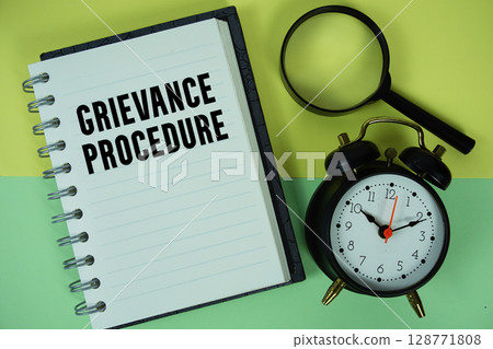Grievance Procedure text written on notebook paper with magnifying glass and alarm clock 128771808