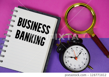 Business Banking text written on notebook paper with magnifying glass and alarm clock 128771812