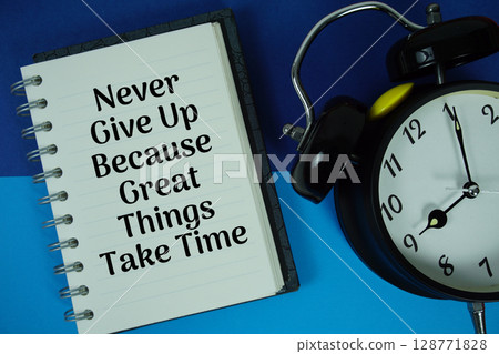 Never Give Up Because Great Things Take Time text written on notebook paper with alarm clock 128771828