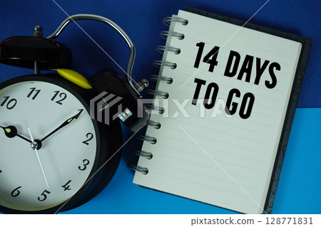 14 Days To Go text written on notebook paper with alarm clock 128771831