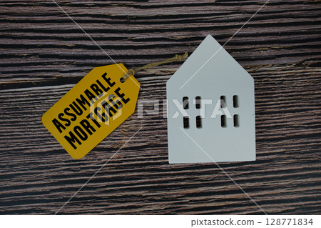 Assumable Mortgage text on price tag with white house model flat lay on wooden background 128771834
