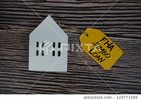 FHA Jumbo Loan text on price tag with white house model flat lay on wooden background FHA Jumbo Loan text on price tag with white house model flat lay on wooden background 128771889