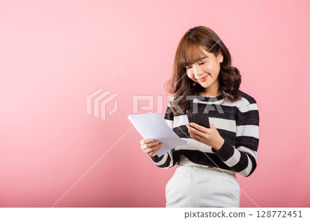 Happy Asian young woman holding mobile smart phone and family budget cost bills document invoice online for payment, Convenience online internet banking. female hold work papernote Happy Asian young woman holding mobile smart phone and family budget cost bills document invoice online for payment, Convenience online internet banking. female hold work papernote 128772451